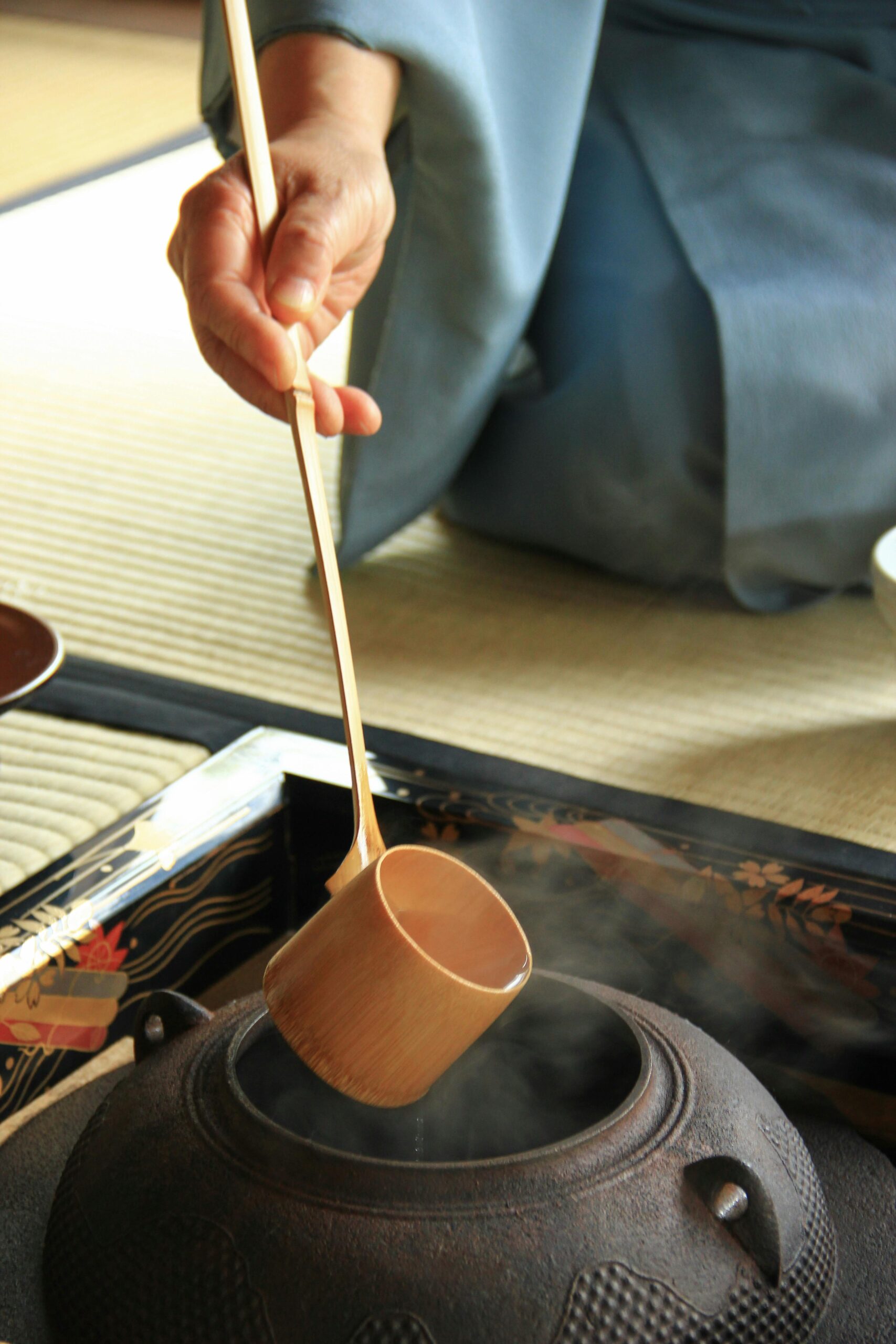 Close-up of a traditional Japanese tea ceremony with a hand holding a water ladle over a steaming pot.