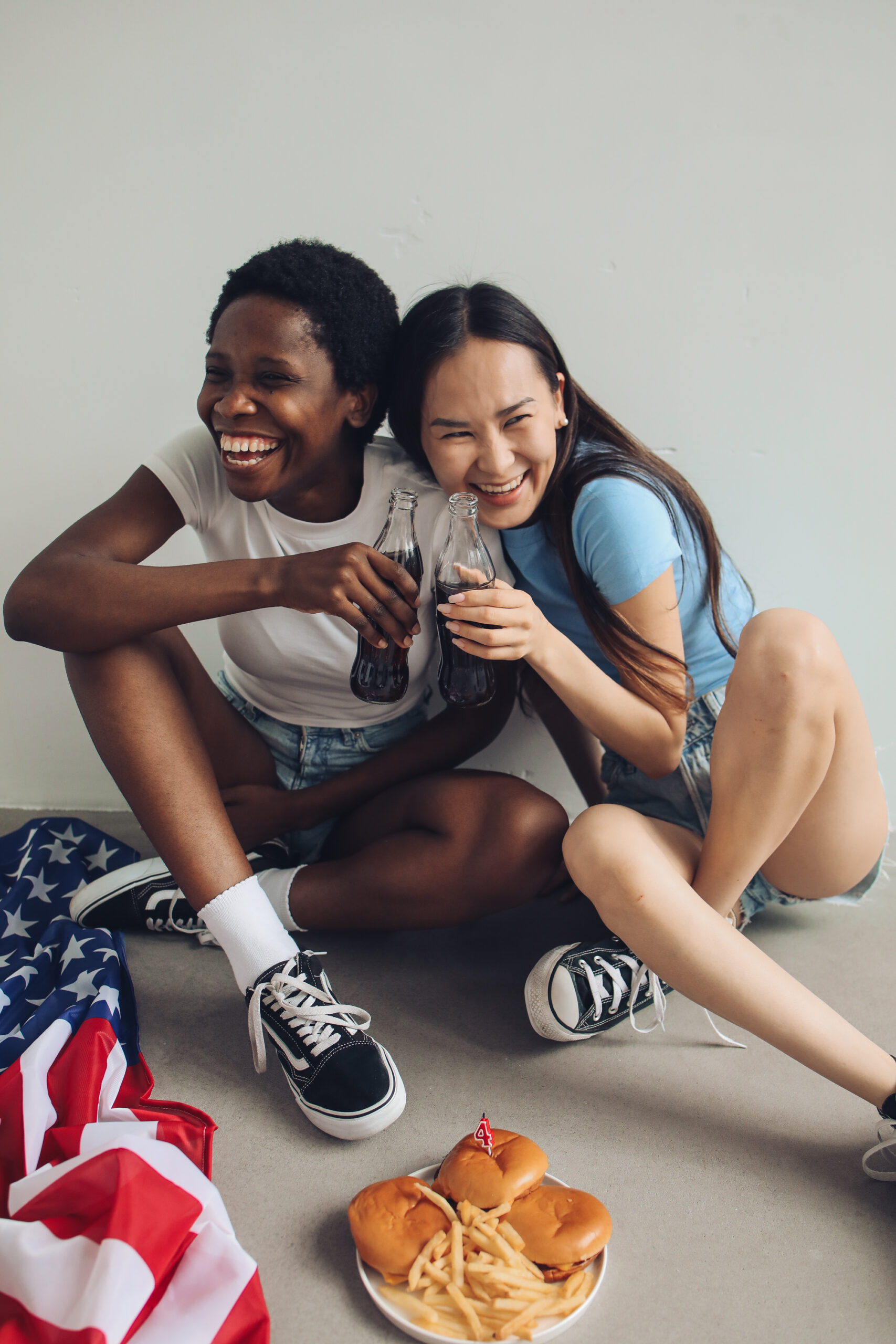 Two friends celebrate indoors with snacks, drinks, and an American flag, enjoying leisure time.
